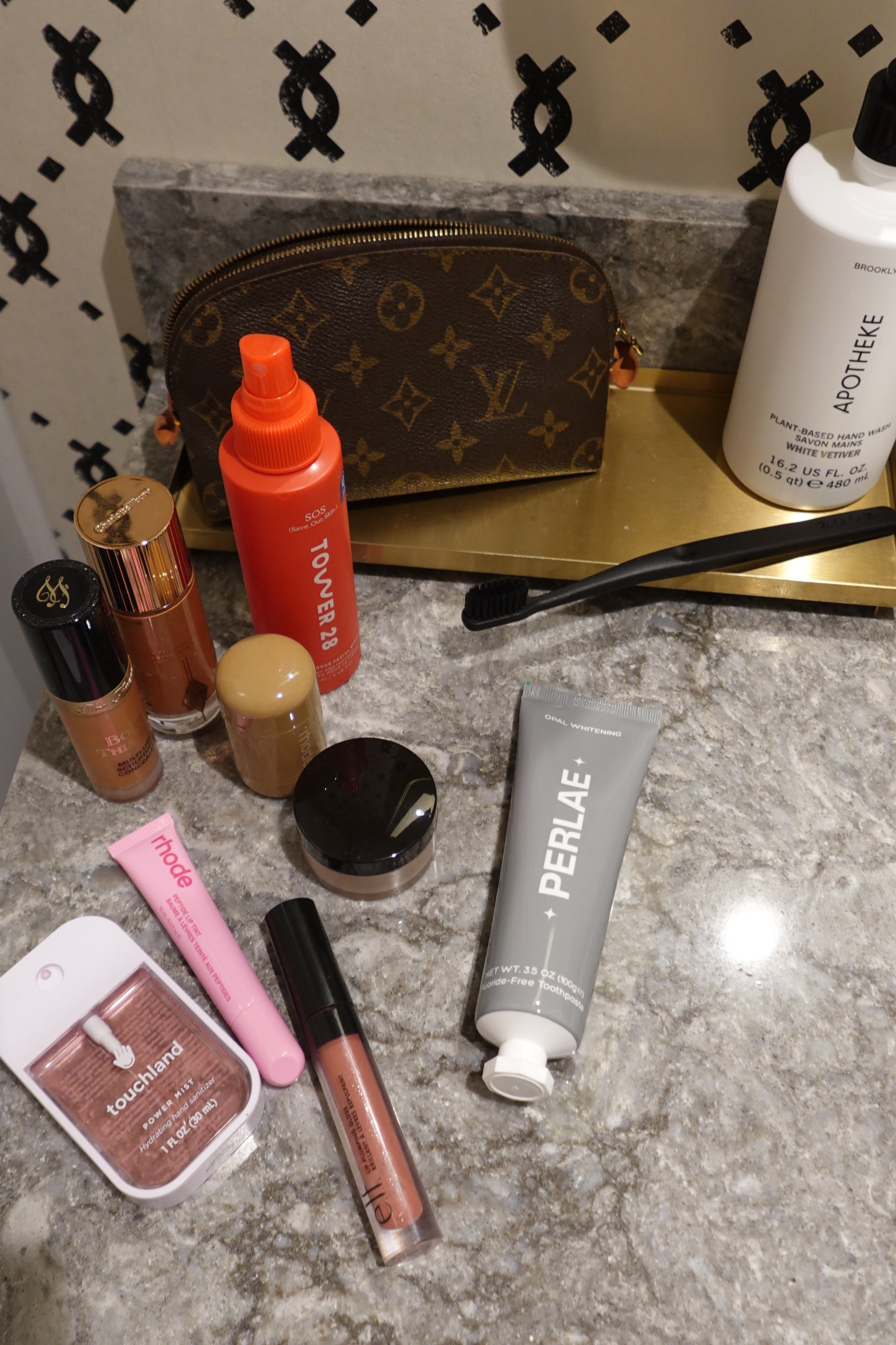Makeup products including lipsticks and a tube of toothpaste on a textured surface with a patterned background.